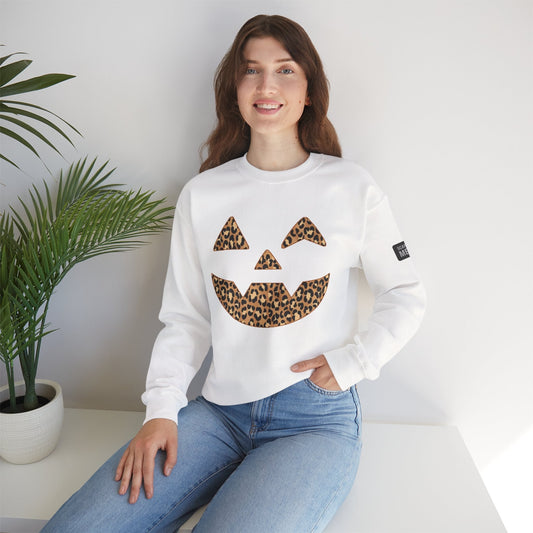 Woman wearing white sweatshirt with leopard print Jack-O'-Lantern face design sitting by table