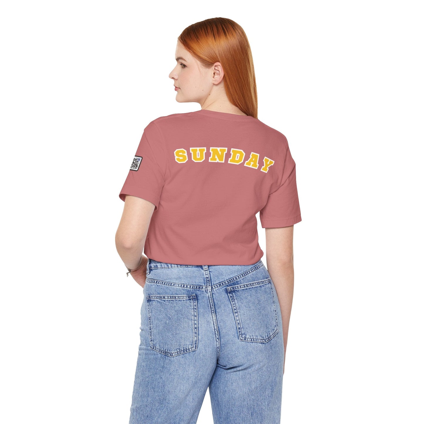 Woman wearing a pink "Sunday" days of the week tee with yellow varsity-style lettering on the back and blue jeans