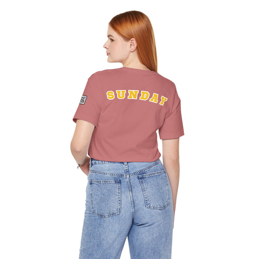 Woman wearing a pink "Sunday" days of the week tee with yellow varsity-style lettering on the back and blue jeans